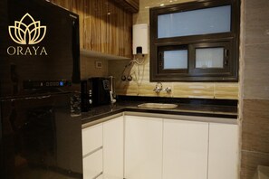 A kitchen with a built-in stove, a coffee maker, and a window with blinds. - Modern and Bright Getaway in Madinaty. (Cairo)