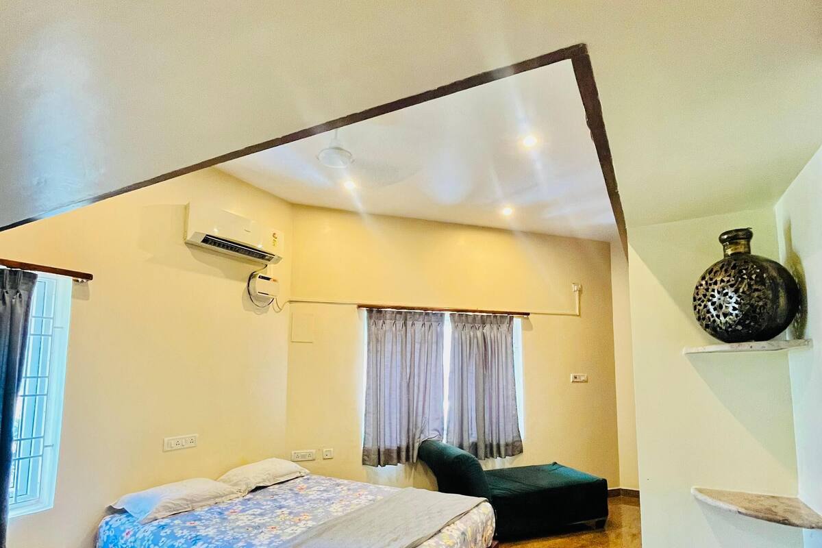 A bedroom with a bed, a small table, a chair, a decorative vase, and a ceiling fan.
