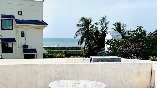 A rooftop terrace with a white building, a view of the sea, and a Panasonic air conditioning unit. - The Tides Inn (Chennai)