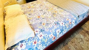 A single bed with a floral bedspread, wooden wardrobe, and a window with curtains. - The Tides Inn (Chennai)