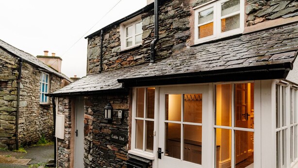 A stone building with a white door and windows, a stone exterior, and a visible interior with wooden flooring and a fireplace.