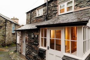 A stone building with a white door and windows, a stone exterior, and a visible interior with wooden flooring and a fireplace.