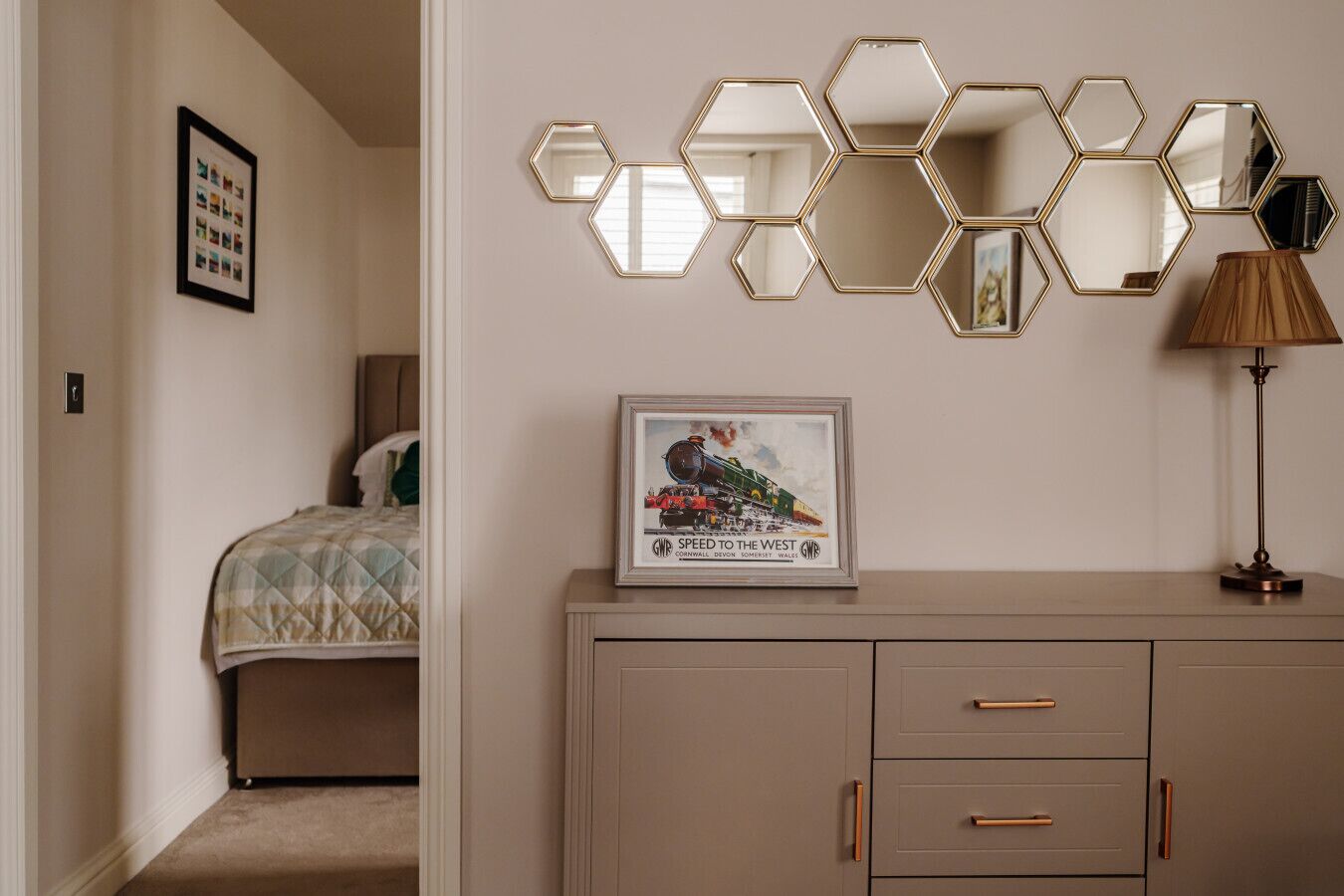 A bedroom with a bed, a dresser with drawers, a lamp, and a wall-mounted mirror.