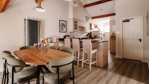A modern kitchen with wooden beams, a dining area with a wooden table and chairs, and a small island with a sink.