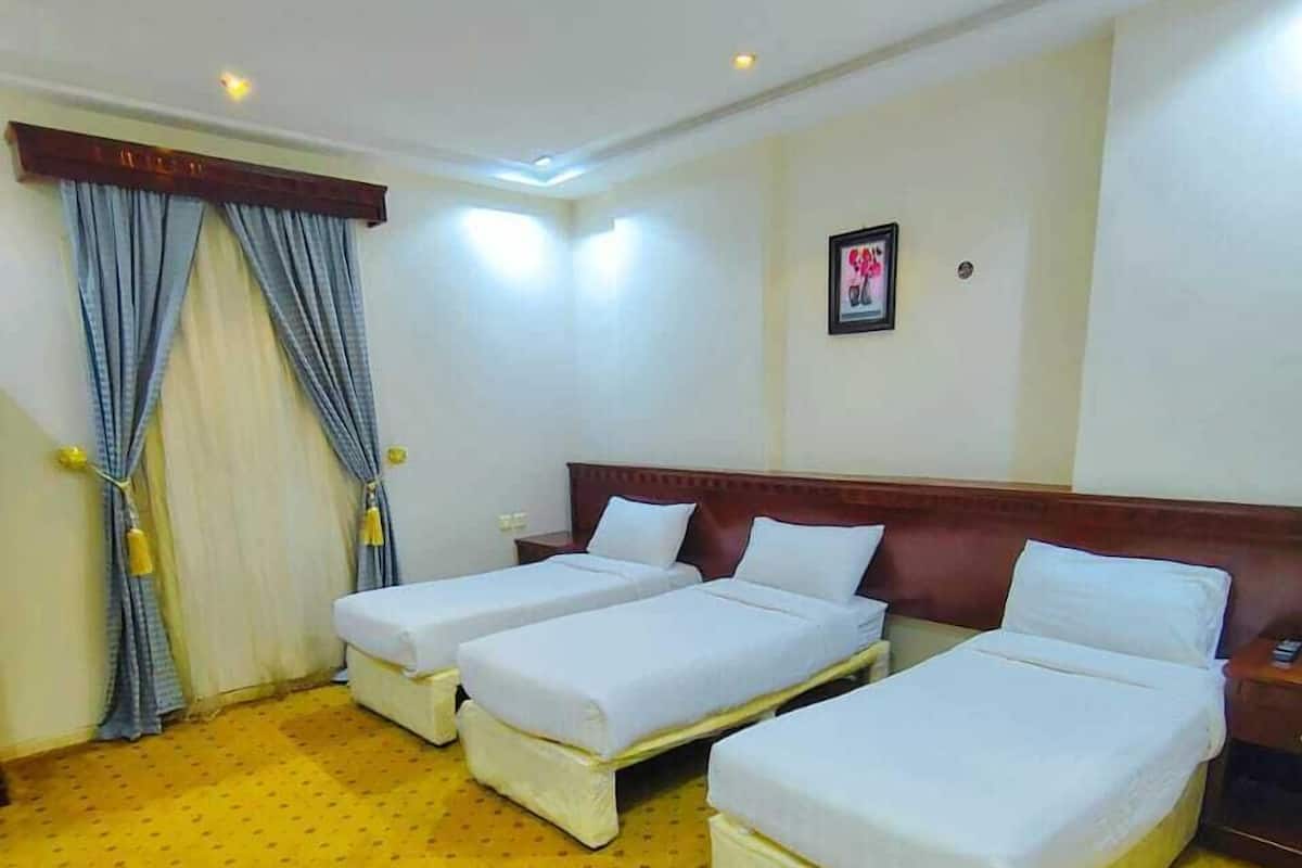 Une chambre d’hôtel avec deux lits simples, une grande fenêtre avec des rideaux et un tapis à motifs jaunes.
