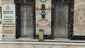 Un hall d’hôtel avec un sol en marbre, deux ascenseurs, une horloge et un panneau d’affichage contenant des informations sur l’hôtel.