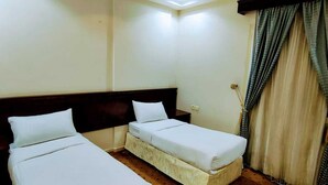 Une chambre d’hôtel avec deux lits simples, une tête de lit en bois, une grande fenêtre avec des rideaux et un sol recouvert de moquette.