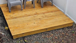 Puisesta laudasta rakennettu terassi, jossa on kaksi Adirondack-tyylistä tuolia ja pieni pöytä.