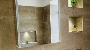 A bathroom with a large mirror, a white sink, and two small shelves with plants.