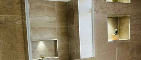 A bathroom with a large mirror, a white sink, and two small shelves with plants.