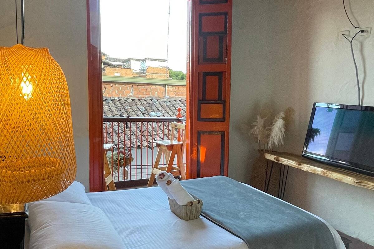 A bedroom with a bed, a TV mounted on the wall, and a balcony with a view of buildings.