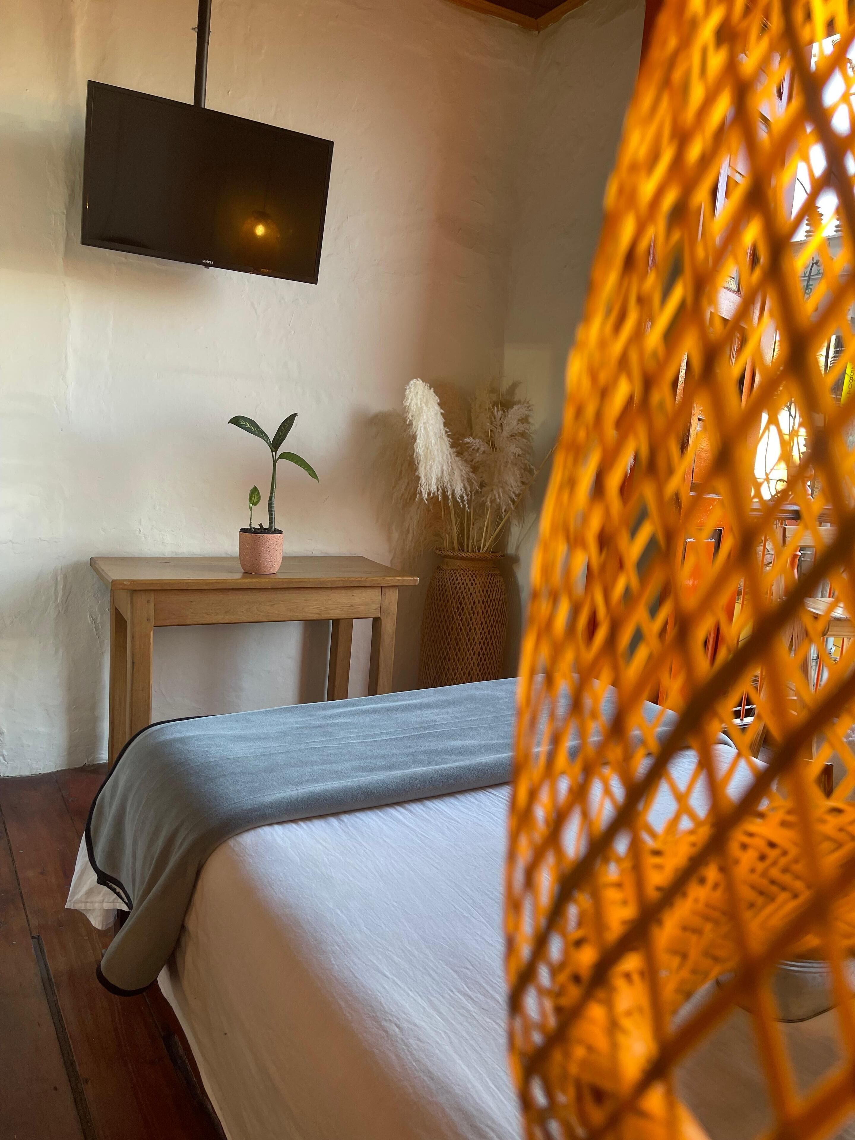Un dormitorio con una cama, una mesita de madera, una planta en maceta y una lámpara colgante.