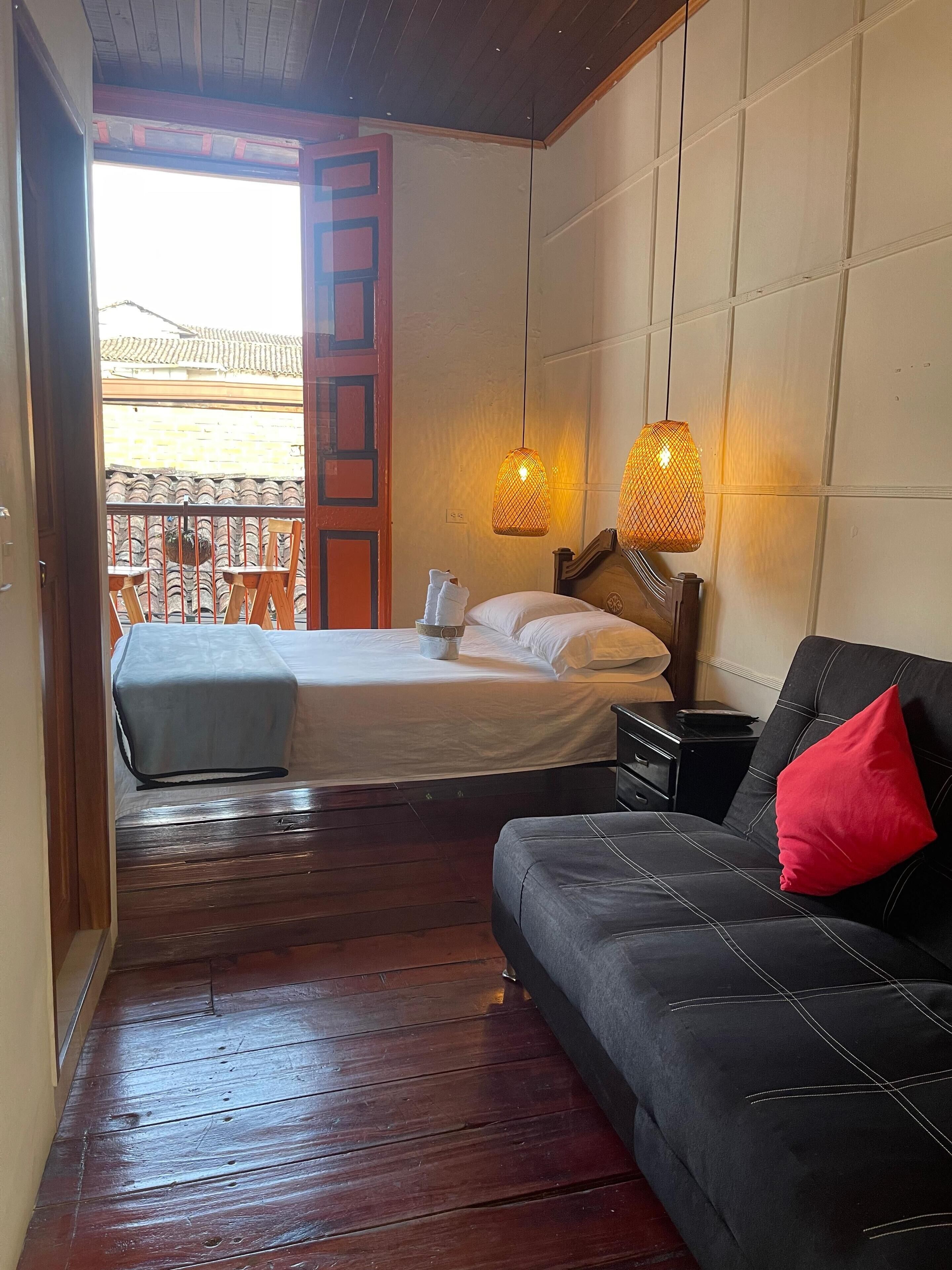 Un dormitorio con cama, sofá y balcón con sillas.