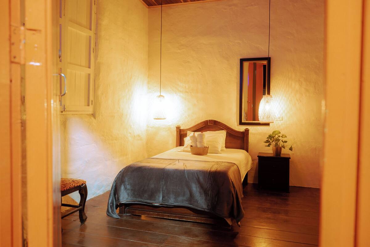 A bedroom with a wooden bed, a bedside table with a plant, and two wall-mounted lamps.