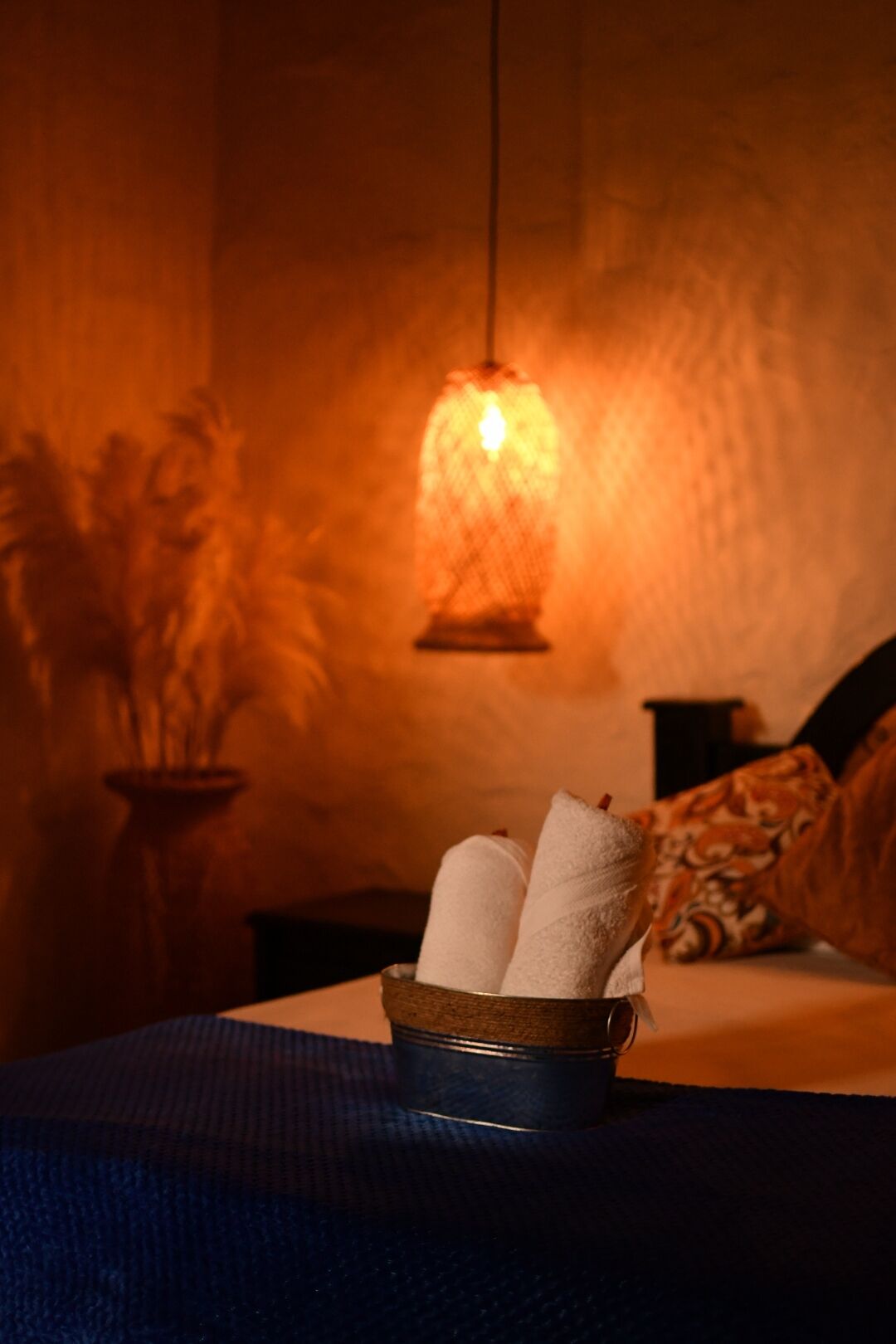 Une pièce avec une lampe suspendue, un récipient en métal contenant des serviettes et un coussin à motifs sur un lit.