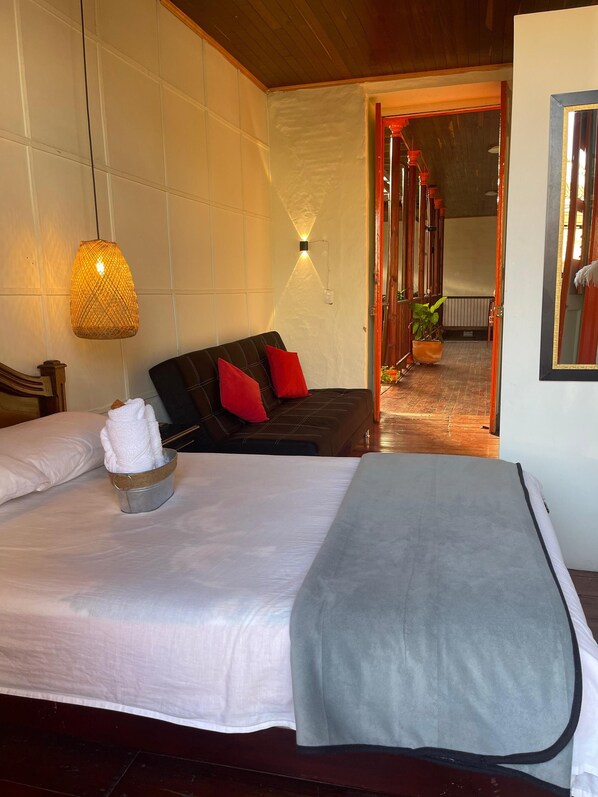 Une chambre d’hôtel avec un lit, une table de chevet sur laquelle se trouve une serviette, une lampe fixée au mur et une vue sur le couloir.