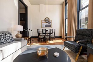 Een moderne woonkamer met een bank, een salontafel, een televisie, een eettafel met stoelen en een groot raam met gordijnen.