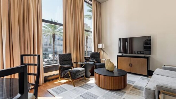 Un salon moderne avec un canapé, un fauteuil, une table basse ronde et un téléviseur posé sur un meuble en bois.
