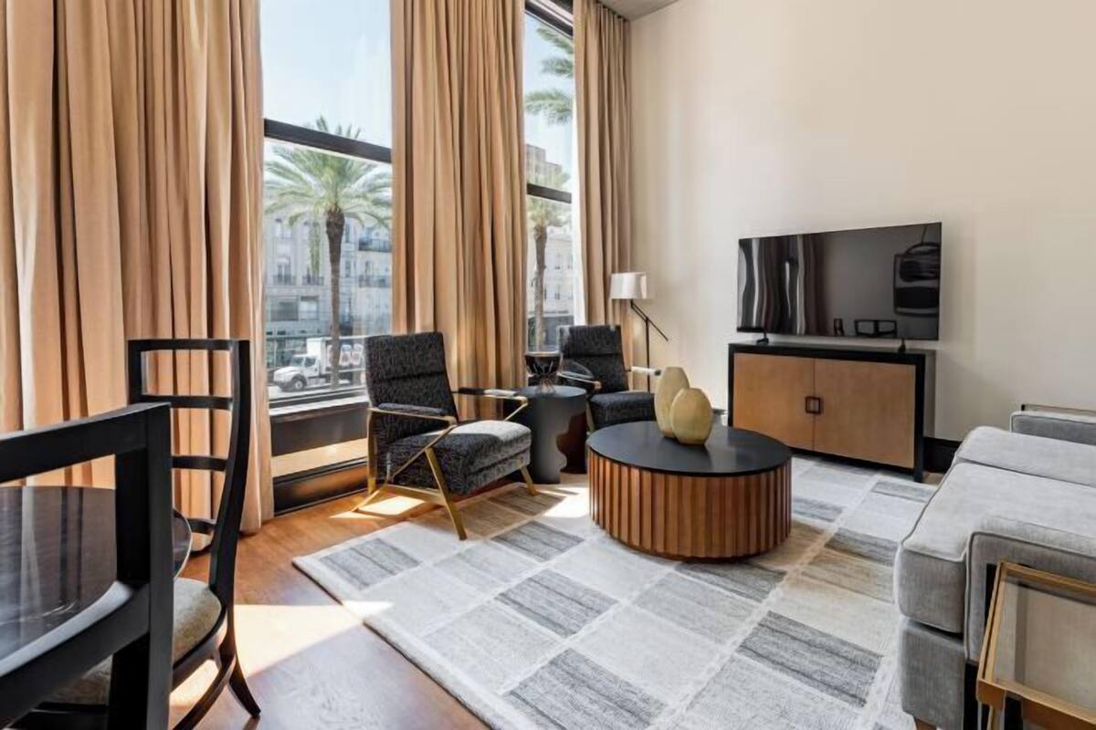 Uma sala de estar moderna com sofá, poltrona, mesa de centro redonda e uma TV em um móvel de madeira.