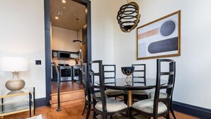 Un coin repas avec une table ronde, des chaises, une lampe et une cuisine en arrière-plan.