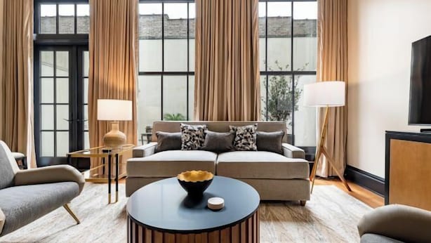A modern living room with a sofa, armchairs, a coffee table, and a TV. - 3BR Group Haven + Private Patio Walk to French Quarter The Mayfair (New Orleans)