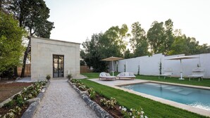 A modern outdoor pool area with a stone building, a gravel pathway, and a well-maintained lawn. - Family Suite - Palazzo Villani Lubelli (Cannole)