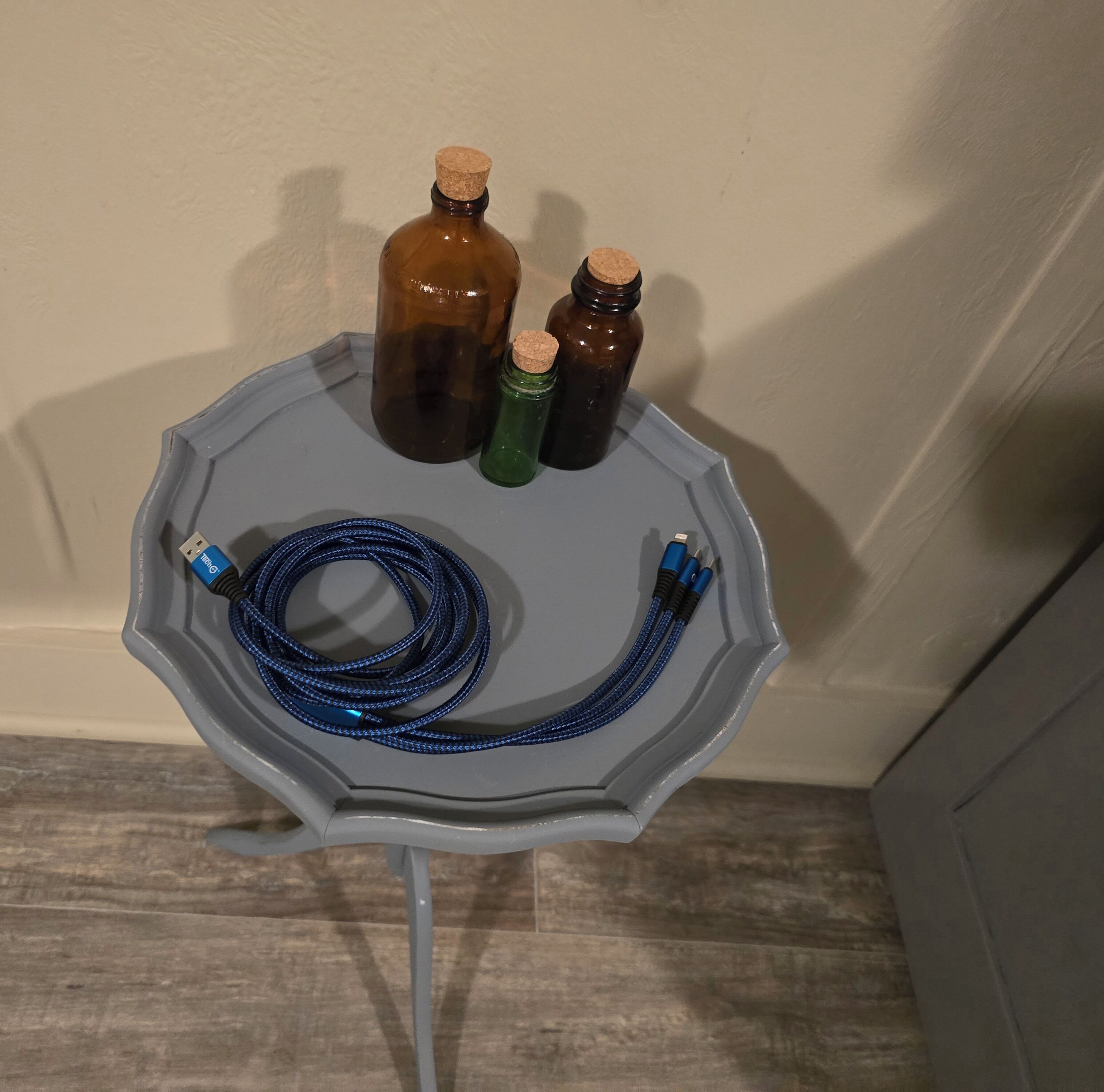 A gray octagonal table with a blue coiled cable, two brown bottles with cork stoppers, and a green bottle with a cork stopper.