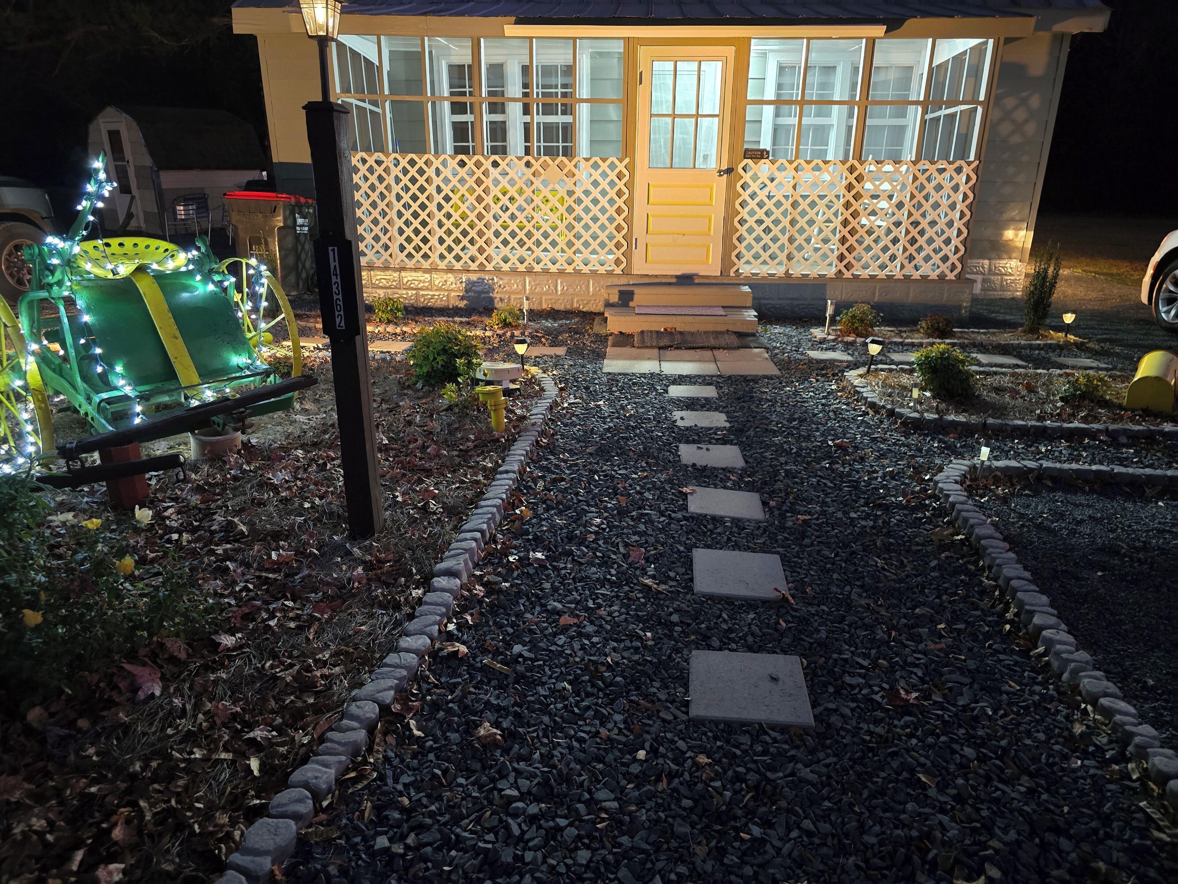 A pathway leading to a house with a wooden fence and a door. There are decorative lights along the path.