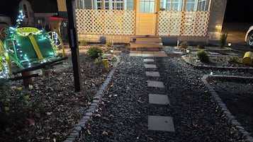 A pathway leading to a house with a wooden fence and a door. There are decorative lights along the path.