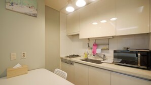 Une cuisine de taille réduite, avec des meubles blancs, une cuisinière à gaz, un évier et un four à micro-ondes.