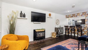 Een woonkamer met een bank, tv, open haard en een keuken die zichtbaar is door een open doorgang.