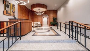 A modern hotel lobby with a marble staircase, wooden paneling, and a reception desk.