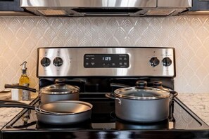 A kitchen with a stainless steel stove, two pots, and a digital clock displaying 12:25. - 2BR Iconic Penthouse Living + Private Patio The Mayfair (New Orleans)