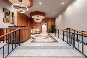 A modern hotel lobby with a curved reception desk, a marble staircase, and a central seating area. - 2BR Iconic Penthouse Living + Private Patio The Mayfair (New Orleans)
