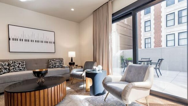 A modern living room with a sofa, armchairs, a coffee table, and a large window with a view of buildings.