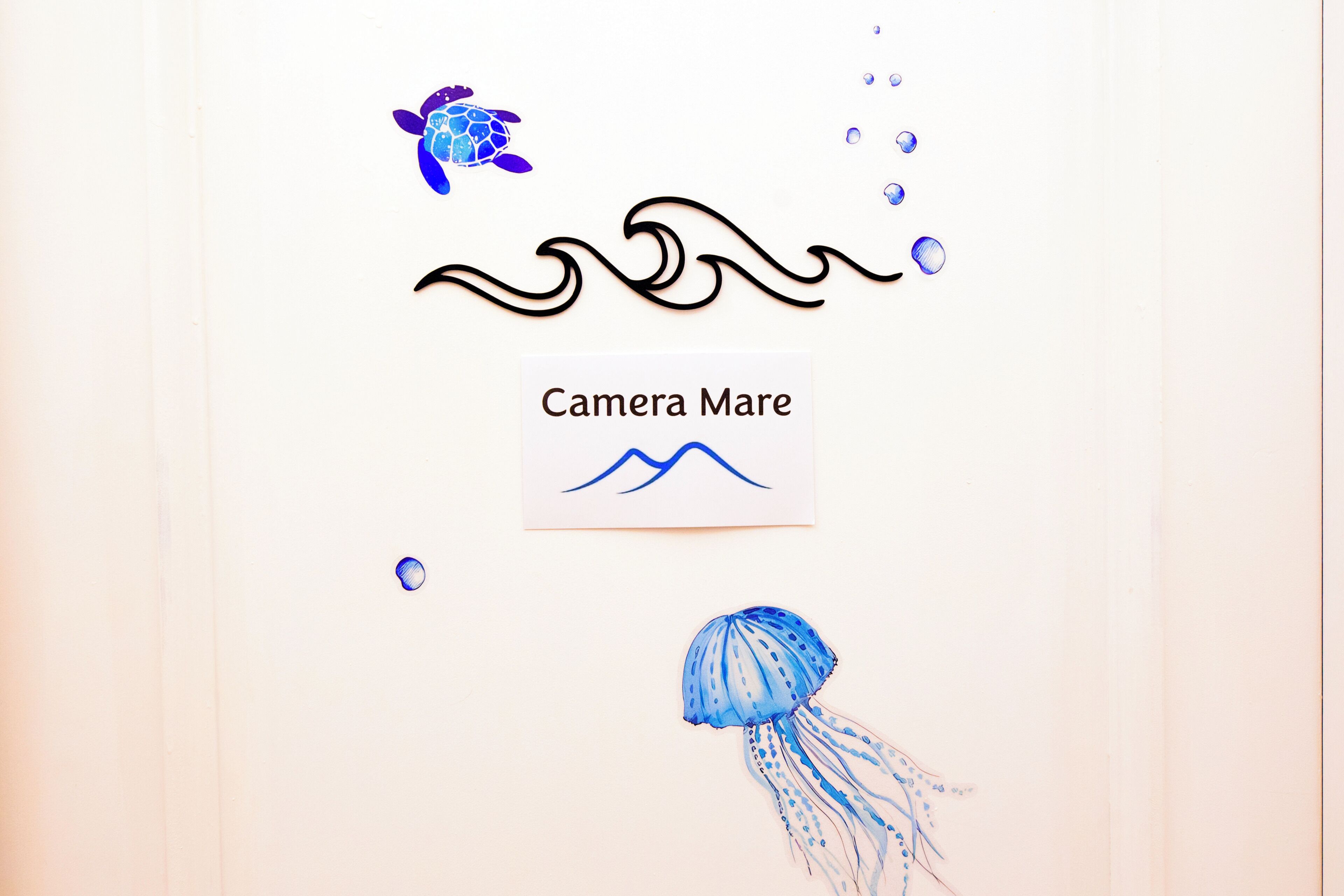 Un mur décoré d’un autocollant représentant une tortue, d’un motif ondulé, d’un autre autocollant représentant une méduse et d’un motif graphique représentant une montagne.