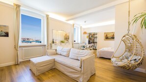 A modern living room with a sectional sofa, a hanging chair, a dining area, and a view of the sea through a large window. - Mare e Monti (Genoa)