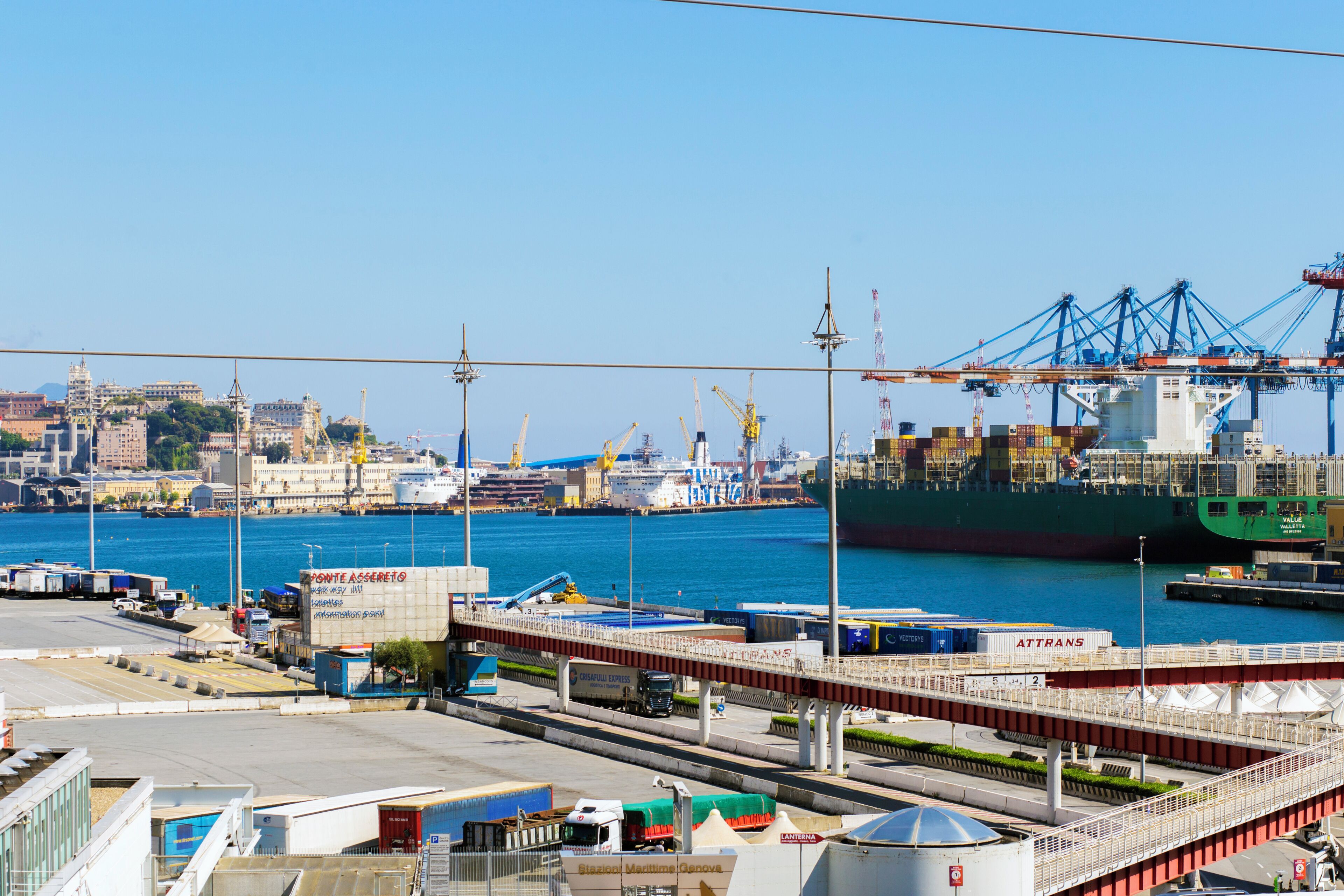 A harbor with a large cargo ship, cranes, and a bridge over the water.