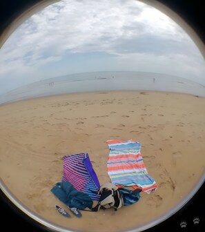 Eine Strandansicht mit zwei Badetüchern und einem Rucksack im Sand.
