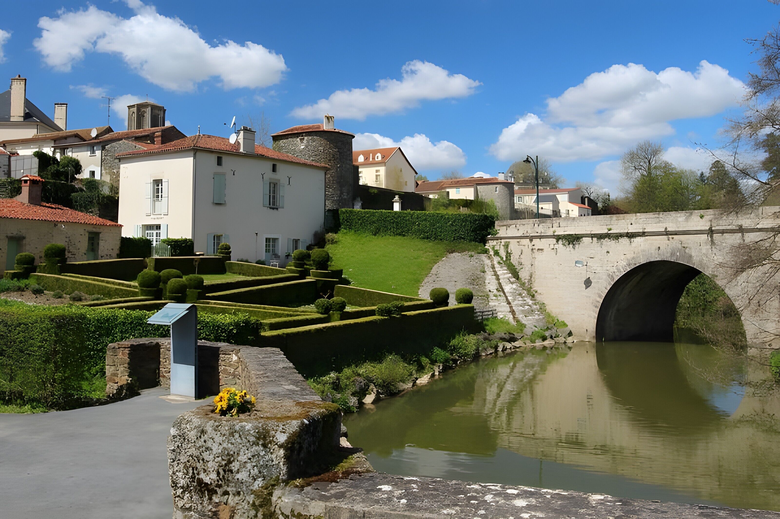 A historic town with a stone bridge, a canal, and well-maintained gardens.