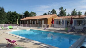 Una piscina con sillas de descanso, un flotador inflable verde y un edificio con tejado de baldosas.