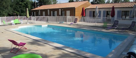A swimming pool with lounge chairs, a green inflatable ring, and a building with a tiled roof.