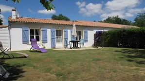 Una casa con techo de tejas, un patio con mesa y sillas, y un tobogán.