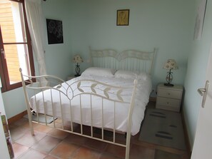 Un dormitorio con cama, dos mesitas de noche, una ventana con cortinas y un cuadro en la pared.