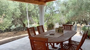 A covered outdoor dining area with a wooden table and chairs, surrounded by stone walls and trees. - Cottage 'Stazzu Spadulagliu near Olbia' with Mountain View, Wi-Fi and Air Conditioning (Telti)