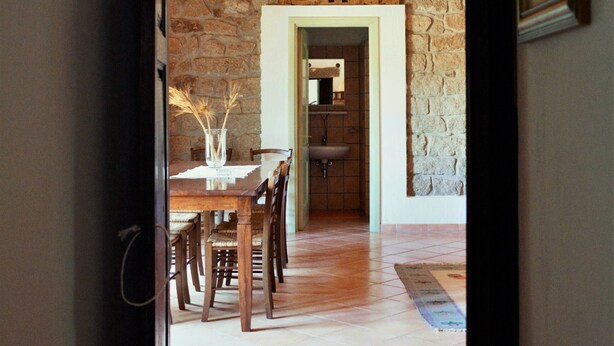 A doorway leading to a dining area with a stone wall, wooden ceiling, and a tiled floor. - Cottage 'Stazzu Spadulagliu near Olbia' with Mountain View, Wi-Fi and Air Conditioning (Telti)