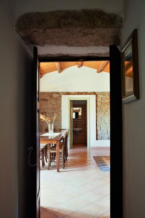 A doorway leading to a dining area with a stone wall, wooden ceiling, and a tiled floor. - Cottage 'Stazzu Spadulagliu near Olbia' with Mountain View, Wi-Fi and Air Conditioning (Telti)