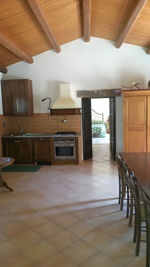 A kitchen with wooden cabinets, a stove, and a dining area with chairs. - Cottage 'Stazzu Spadulagliu near Olbia' with Mountain View, Wi-Fi and Air Conditioning (Telti)