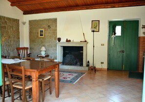 A dining area with a wooden table and chairs, a fireplace, a stone wall, and a green door. - Cottage 'Stazzu Spadulagliu near Olbia' with Mountain View, Wi-Fi and Air Conditioning (Telti)