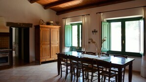 A dining area with a wooden table and chairs, a cabinet, and a window with green shutters. - Cottage 'Stazzu Spadulagliu near Olbia' with Mountain View, Wi-Fi and Air Conditioning (Telti)